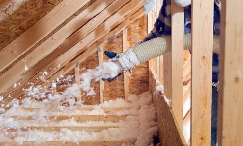 Worker Spraying Blown Fiberglass Insulation between Attic Trusses