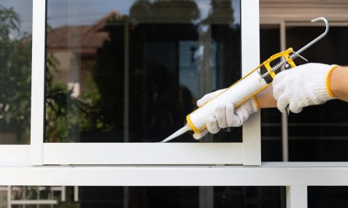 Construction worker using silicone sealant caulk for repair leaked inside window frame.